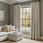 Cozy living room with plaid-patterned beige curtains, a white sofa, and a matching ottoman by large windows.